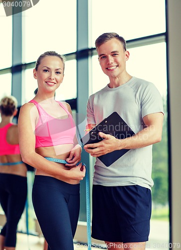 Image of smiling young woman with personal trainer in gym