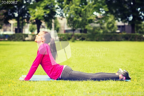Image of smiling woman doing exercises on mat outdoors
