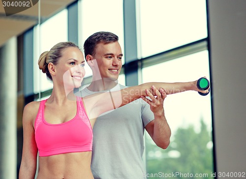 Image of smiling young woman with personal trainer in gym