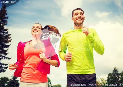 Image of smiling couple with earphones running outdoors