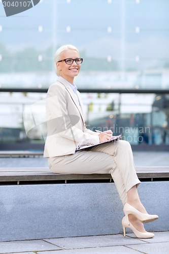 Image of young smiling businesswoman with notepad outdoors