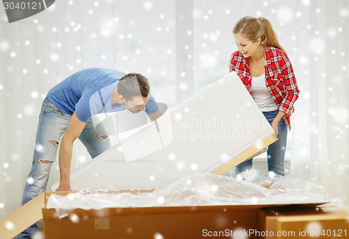 Image of smiling couple opening big cardboard box with sofa