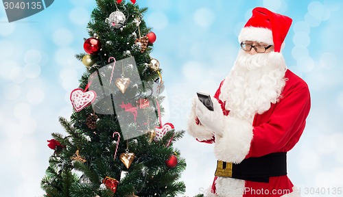 Image of santa claus with smartphone and christmas tree