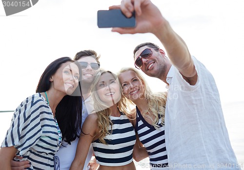 Image of happy friends on beach and taking selfie