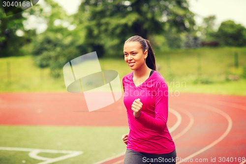 Image of smiling young woman running on track outdoors