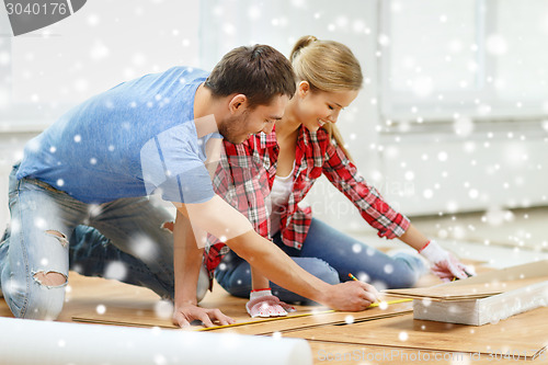 Image of smiling couple measuring wood flooring