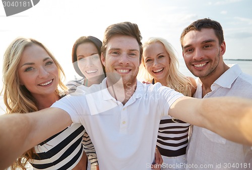 Image of happy friends on beach and taking selfie