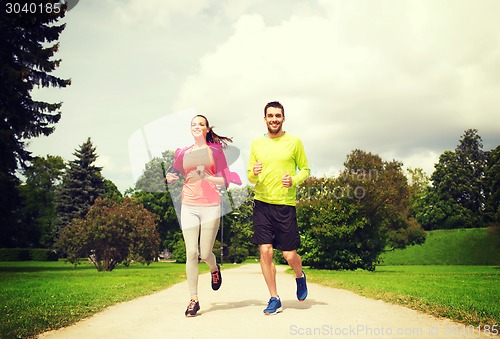 Image of smiling couple with earphones running outdoors