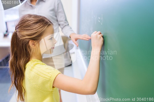 Image of little smiling schoolgirl writing on chalk board