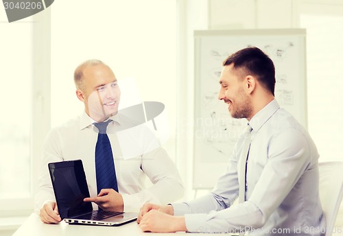 Image of two smiling businessmen with laptop in office