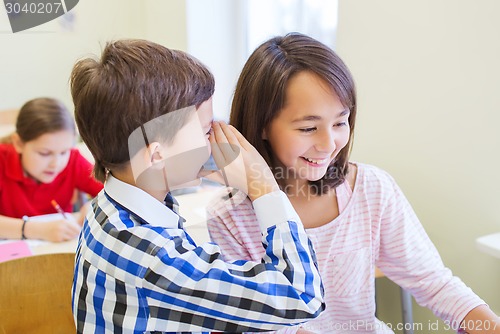 Image of smiling schoolboy whispering to classmate ear