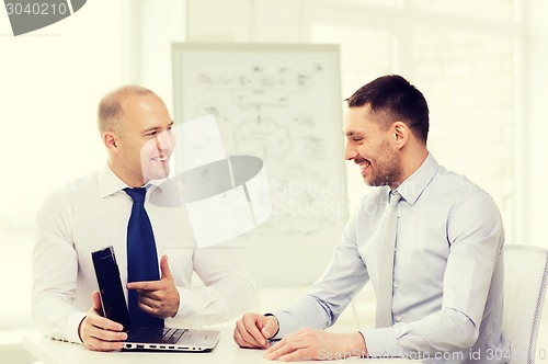 Image of two smiling businessmen with laptop in office