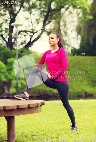 Image of smiling woman stretching on bench outdoors