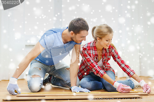 Image of smiling couple measuring wood flooring