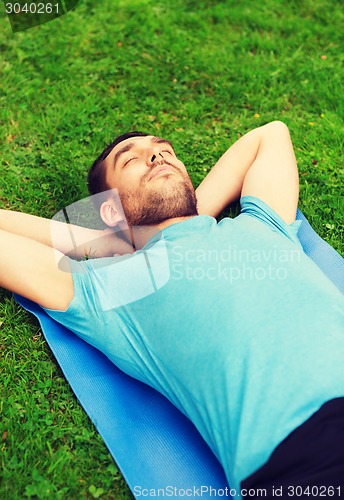 Image of smiling man lying on mat outdoors