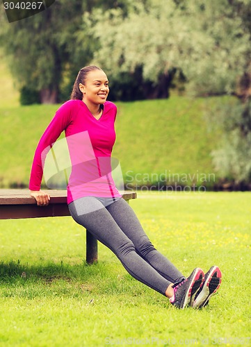 Image of smiling woman doing push-ups on bench outdoors