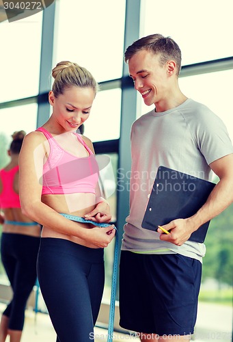 Image of smiling young woman with personal trainer in gym