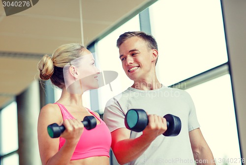 Image of smiling young woman with personal trainer in gym