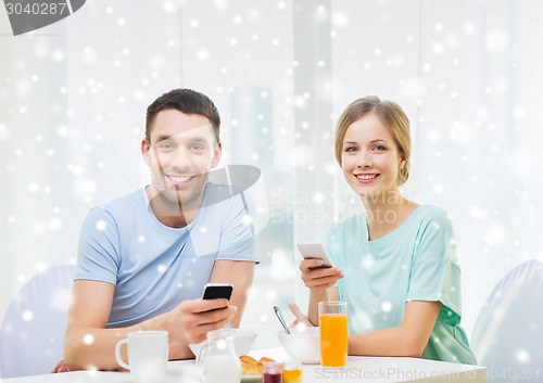 Image of smiling couple with smartphones having breakfast