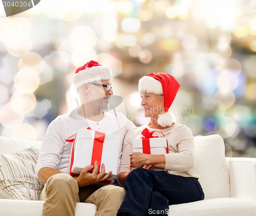 Image of happy senior couple in santa hats with gift boxes