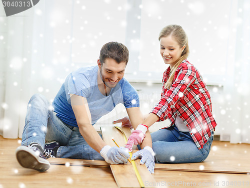 Image of smiling couple measuring wood flooring