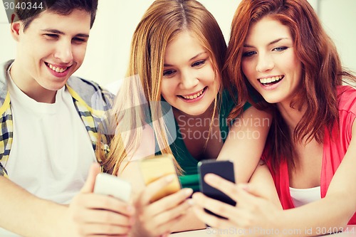 Image of three smiling students with smartphone at school