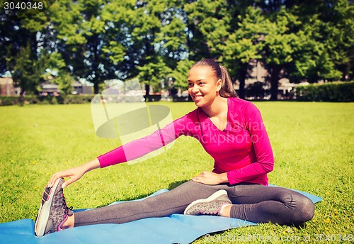 Image of smiling woman stretching leg on mat outdoors