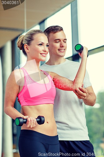 Image of smiling young woman with personal trainer in gym