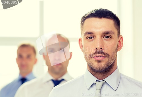 Image of serious businessman in office with team on back