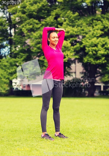 Image of smiling black woman stretching leg outdoors