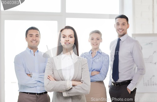 Image of smiling businesswoman in office with team on back