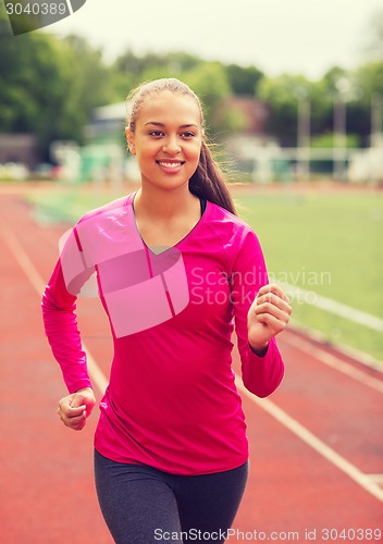 Image of smiling young woman running on track outdoors