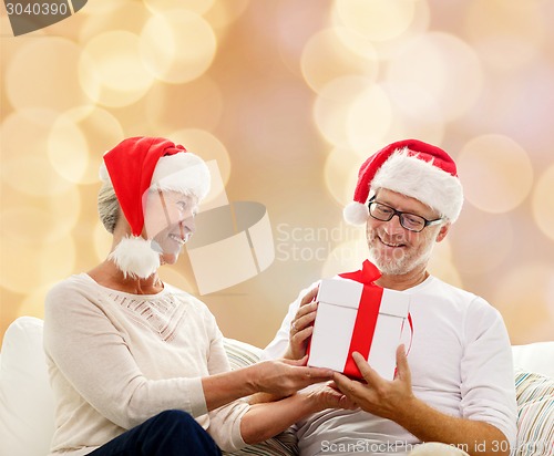 Image of happy senior couple in santa hats with gift box