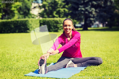 Image of smiling woman stretching leg on mat outdoors