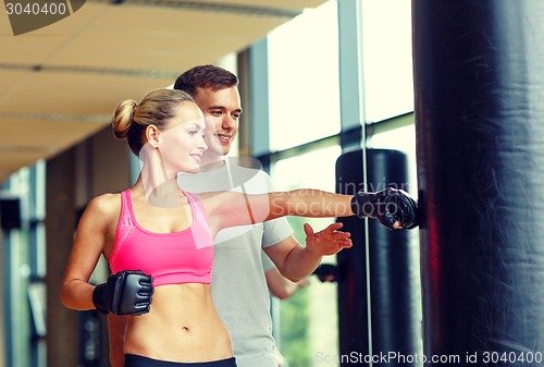 Image of smiling woman with personal trainer boxing in gym