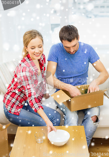 Image of smiling couple opening cardboard box with dishes