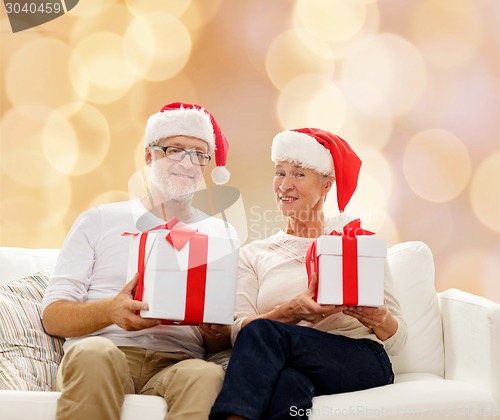 Image of happy senior couple in santa hats with gift boxes