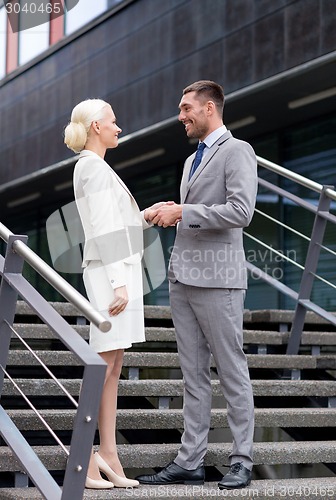 Image of smiling businessmen shaking hands on street