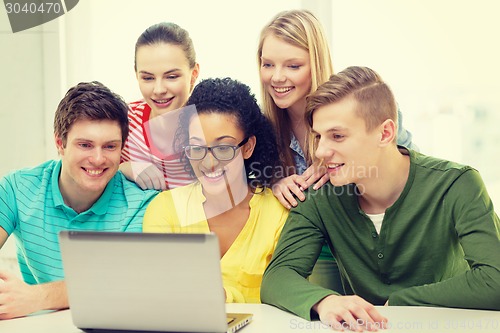 Image of smiling students looking at laptop at school