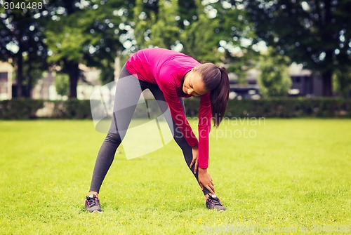 Image of smiling black woman stretching leg outdoors