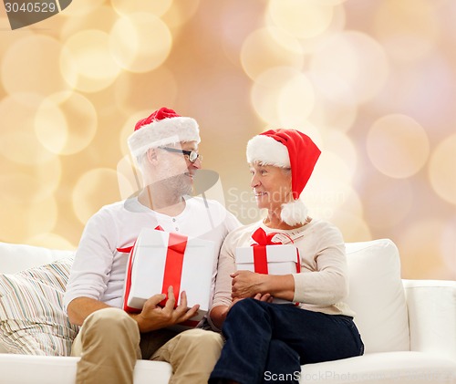 Image of happy senior couple in santa hats with gift boxes