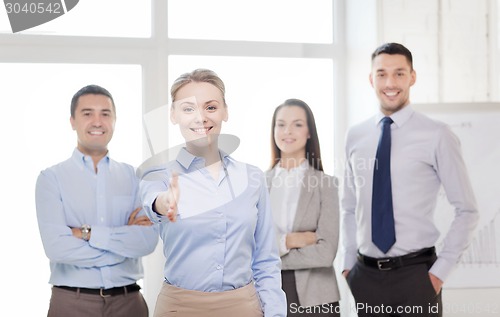 Image of smiling businesswoman in office with team on back