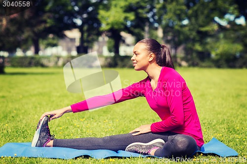 Image of smiling woman stretching leg on mat outdoors