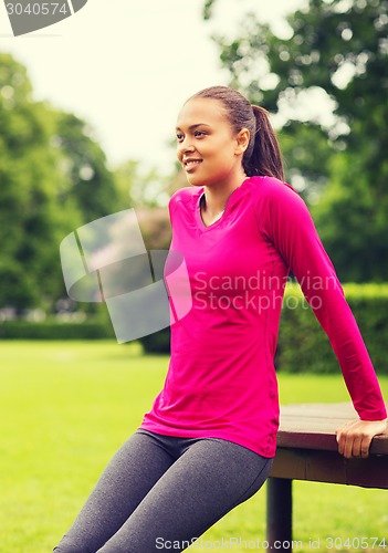 Image of smiling woman doing push-ups on bench outdoors