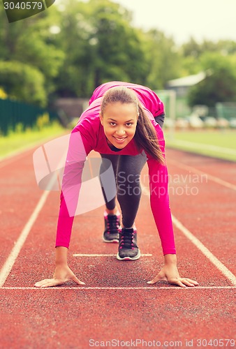 Image of smiling young woman running on track outdoors