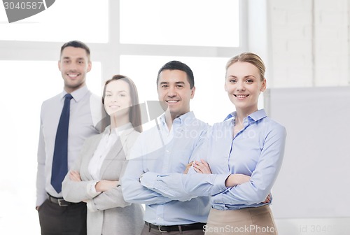 Image of smiling businesswoman in office with team on back