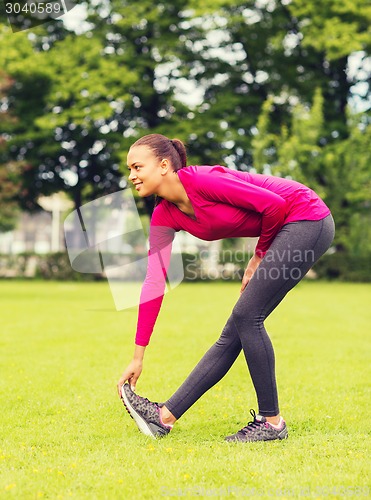 Image of smiling black woman stretching leg outdoors