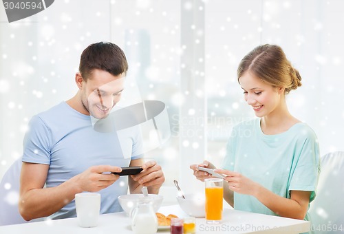 Image of smiling couple with smartphones having breakfast