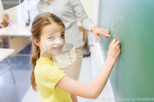 Image of little smiling schoolgirl writing on chalk board