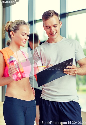 Image of smiling young woman with personal trainer in gym